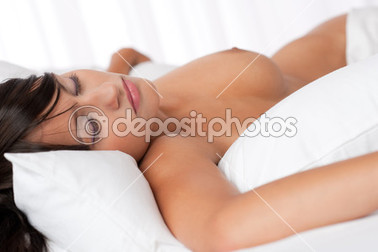 Beyaz yatakta çıplak uyuyan kahverengi saçlı kadın